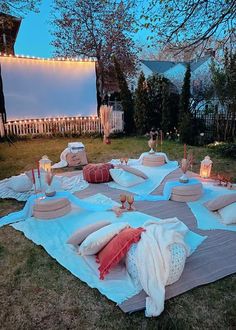 an outdoor movie is set up with pillows and blankets on the grass in front of a fence