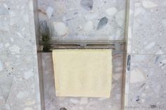 a yellow towel hanging on the wall next to a white tiled shower stall with rocks and plants