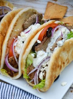 three tacos with meat and vegetables on a plate next to tortilla chips