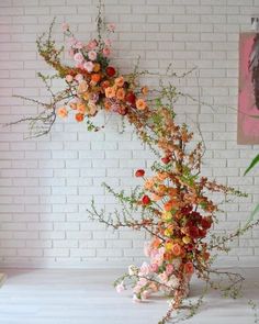 an arrangement of flowers in a vase against a brick wall