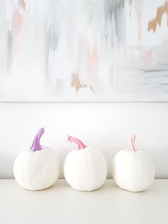 three white pumpkins sitting on top of a table next to each other in front of a painting