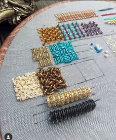 a close up of a cross stitch pattern on a piece of cloth with beads and pins