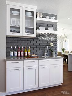 a kitchen with white cabinets and gray brick wall behind the countertop is filled with wine glasses