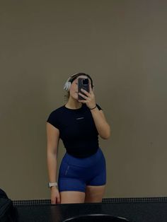 a woman taking a selfie in front of a mirror wearing blue shorts and headphones