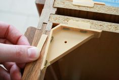 a hand holding a piece of wood near a drawer