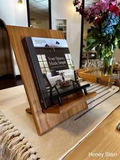 a table with a book on it and flowers in vases behind the bookshelf