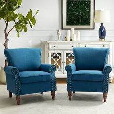 two blue chairs sitting next to each other in front of a white dresser and potted plant