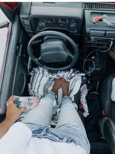 a person sitting in the driver's seat of a car with their feet on the steering wheel