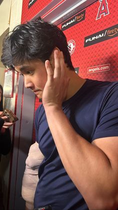 a man holding his hand to his ear while standing in front of a red wall