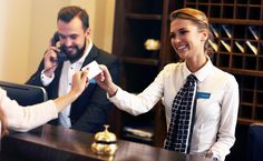 a man and woman are shaking hands in front of a hotel reception desk, while another person is on the phone