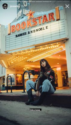 a woman sitting on the ground in front of a movie theater with her legs crossed