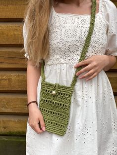 a woman wearing a white dress holding a green crocheted purse in front of a wooden wall