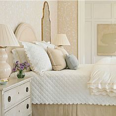 a white bed sitting in a bedroom next to a dresser and lamps on either side of it