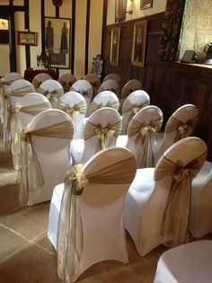 rows of white chairs with bows and sashes on them in a banquet hall setting