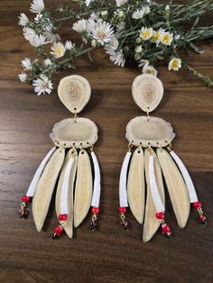 two pairs of white and red earrings on a wooden table with flowers in the background