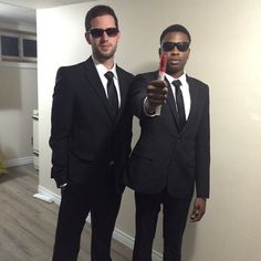 two men dressed in suits and sunglasses are posing for the camera while holding a red object