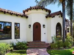 a white stucco house with brown trim and arched windows, palm trees, and steps leading up to the front door