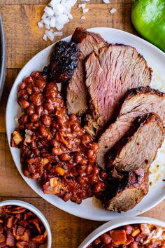 some meat and beans are on a white plate next to green peppers, limes and onions