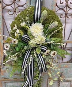 a wreath with white flowers and greenery hanging on a door