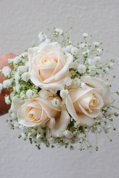 a bouquet of white roses and baby's breath is being held by a hand