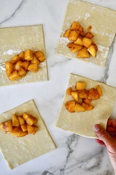 four uncooked pieces of fruit are on top of floured dough and being held by someone's hand