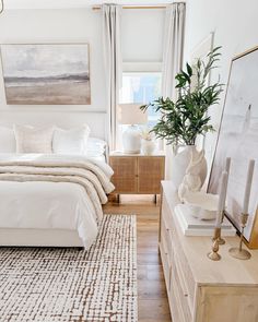 a bedroom with white bedding and wooden dressers, paintings on the wall above it