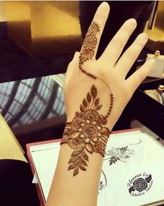 a woman's hand with henna tattoos on it, and a flower design on the wrist