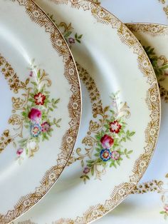 four plates with floral designs on them sitting side by side in a row, one is white and the other has gold trim