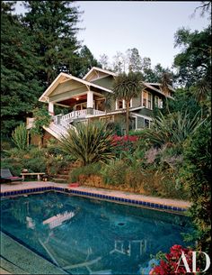 an outdoor swimming pool surrounded by greenery and trees with steps leading up to the house