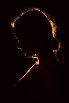 the silhouette of a woman's head against a dark background with light coming through her hair