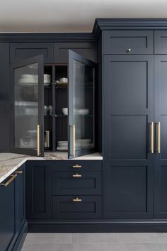 a kitchen with dark blue cabinets and marble counter tops, gold pulls on the doors