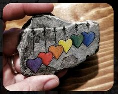 someone is holding a rock with hearts painted on it and arrows hanging from the rocks