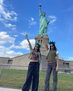 two women standing next to each other in front of the statue of liberty holding up their hands