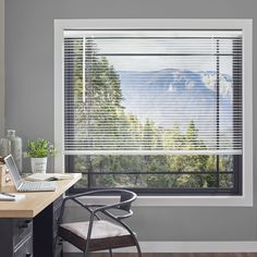 a desk with a computer and chair in front of a window that has mountains outside