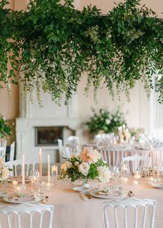 the tables are set with white linens and greenery hanging from the ceiling above them