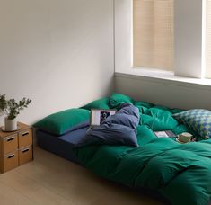 an unmade bed with green sheets and pillows in a white room next to a window