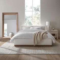 a white bed sitting in a bedroom next to a mirror and table with two vases on it