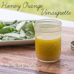 a jar of honey orange vinaigrette next to a plate of spinach