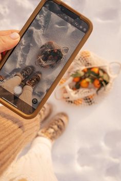 someone taking a photo with their cell phone while standing in the snow next to some oranges