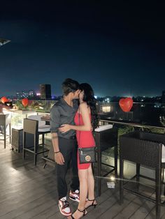 a man and woman are kissing on a balcony at night with the city lights in the background