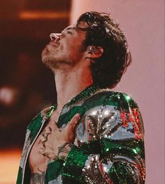 a man with his hand on his chest wearing a sequin jacket and looking up into the sky