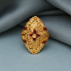 an ornate gold ring with red stones on the center sits atop a gray fabric background