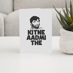 a card that says kitne aadm the on it next to a potted plant