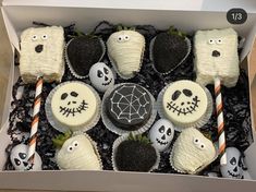 an open box filled with halloween cupcakes and decorated strawberries in black and white frosting