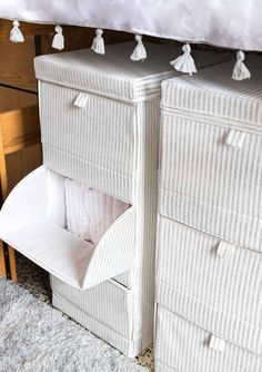 two white drawers with tassels on top of them in front of a bed