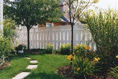 a white fenced in yard next to trees and grass with yellow flowers on the ground