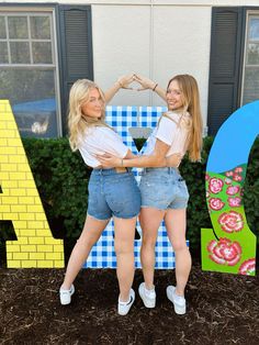 two young women standing next to each other in front of a wall with letters on it