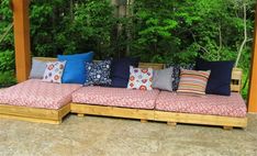 a couch made out of wooden pallets with pillows on it in front of some trees