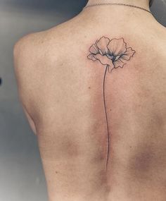 a woman's back with a single flower tattoo on it