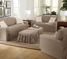 a living room with couches and chairs covered in tan furniture covers on the floor